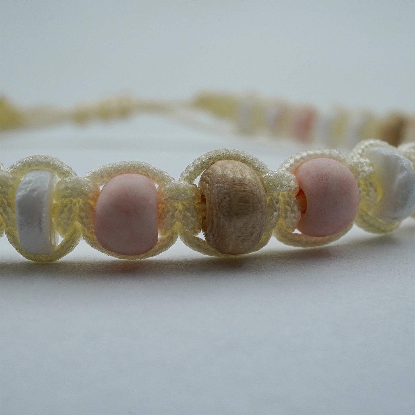 Close-up view of the Coastal Harmony Anklet, highlighting the fine detail of its shell, wood, and pastel glass beads. The sliding knot closure and artisanal textures reveal the careful handmade craftsmanship from Bali.