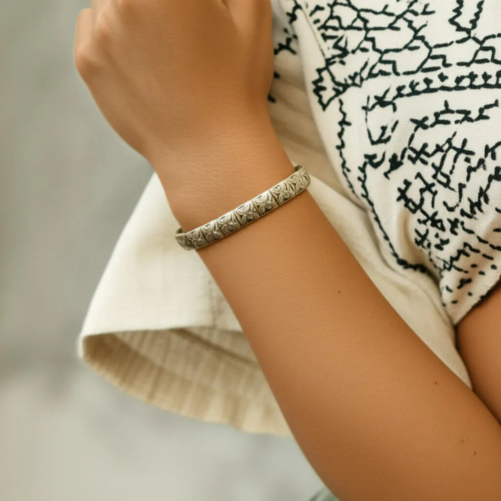 Woman wearing handmade botanical silver bracelet with engraved floral beads in casual setting.