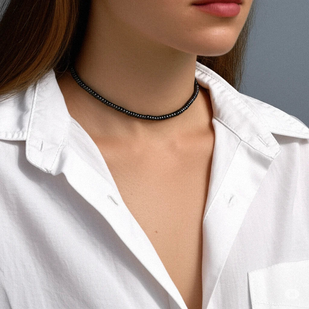 Woman wearing a black bead choker necklace by Camins, styled with a white shirt—minimalist, handmade fashion jewelry inspired by Mediterranean elegance.