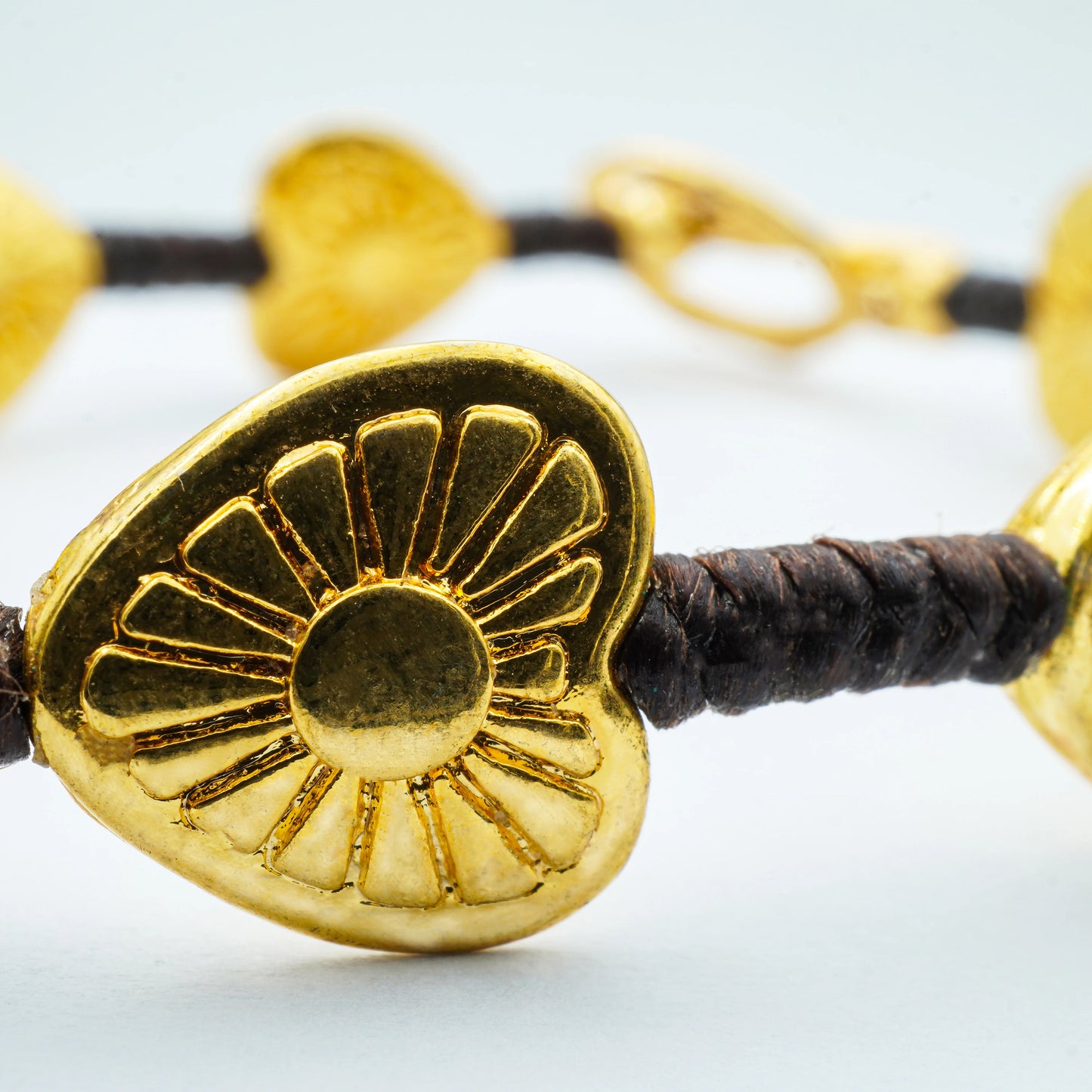 Close-up of the Golden Blossom Hearts Bracelet showcasing delicate gold-toned heart charms on a black cord—handmade in Bali with radiant artisanal detail.