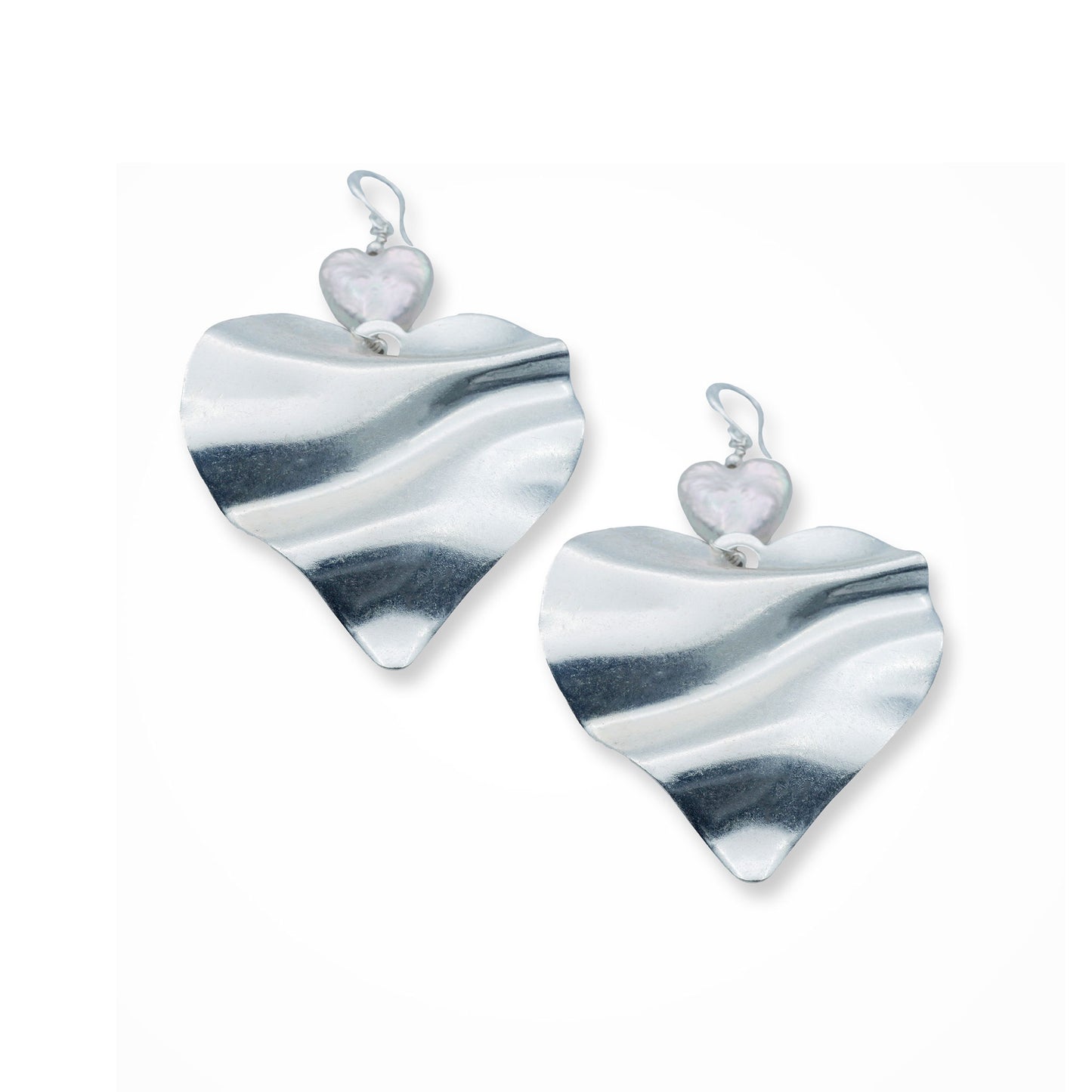 Close-up front view of a woman wearing silver heart pearl earrings with a sculptural double-heart design, capturing a bold romantic style in a soft Mediterranean light. Elegant statement jewelry with a modern boho twist.