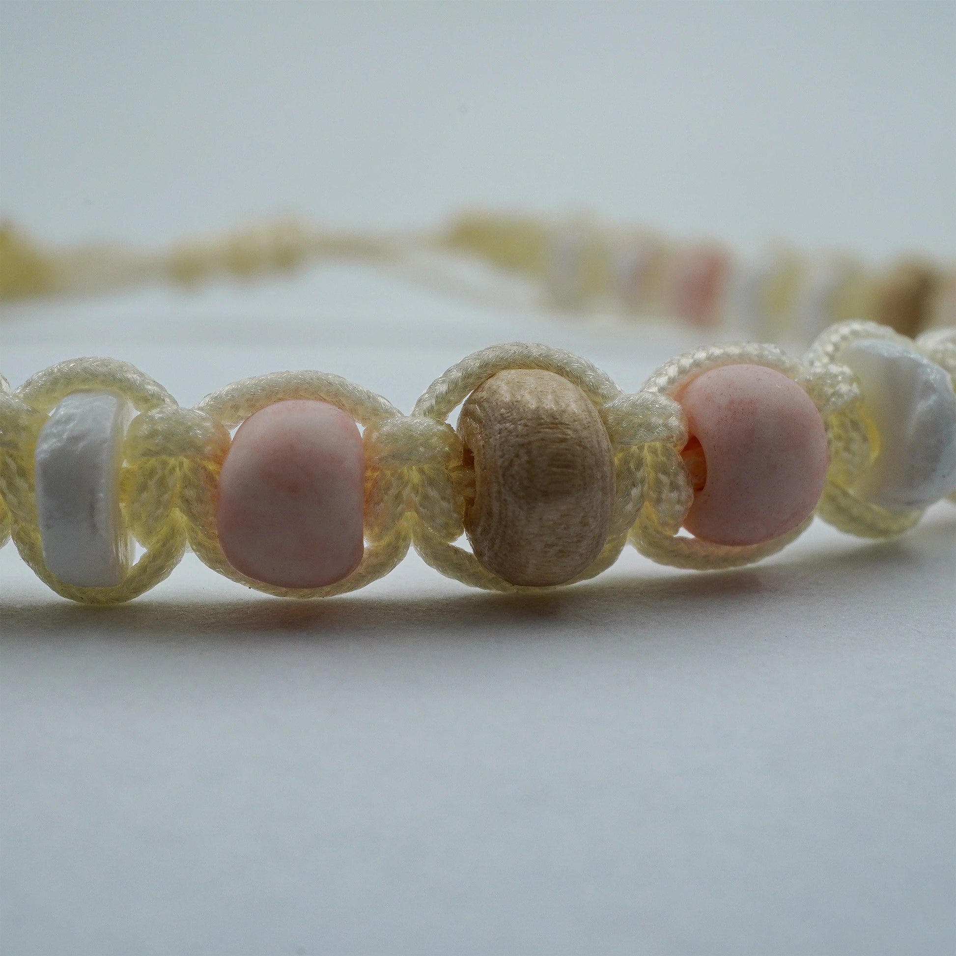 Close-up view of the Coastal Harmony Anklet, highlighting the fine detail of its shell, wood, and pastel glass beads. The sliding knot closure and artisanal textures reveal the careful handmade craftsmanship from Bali.