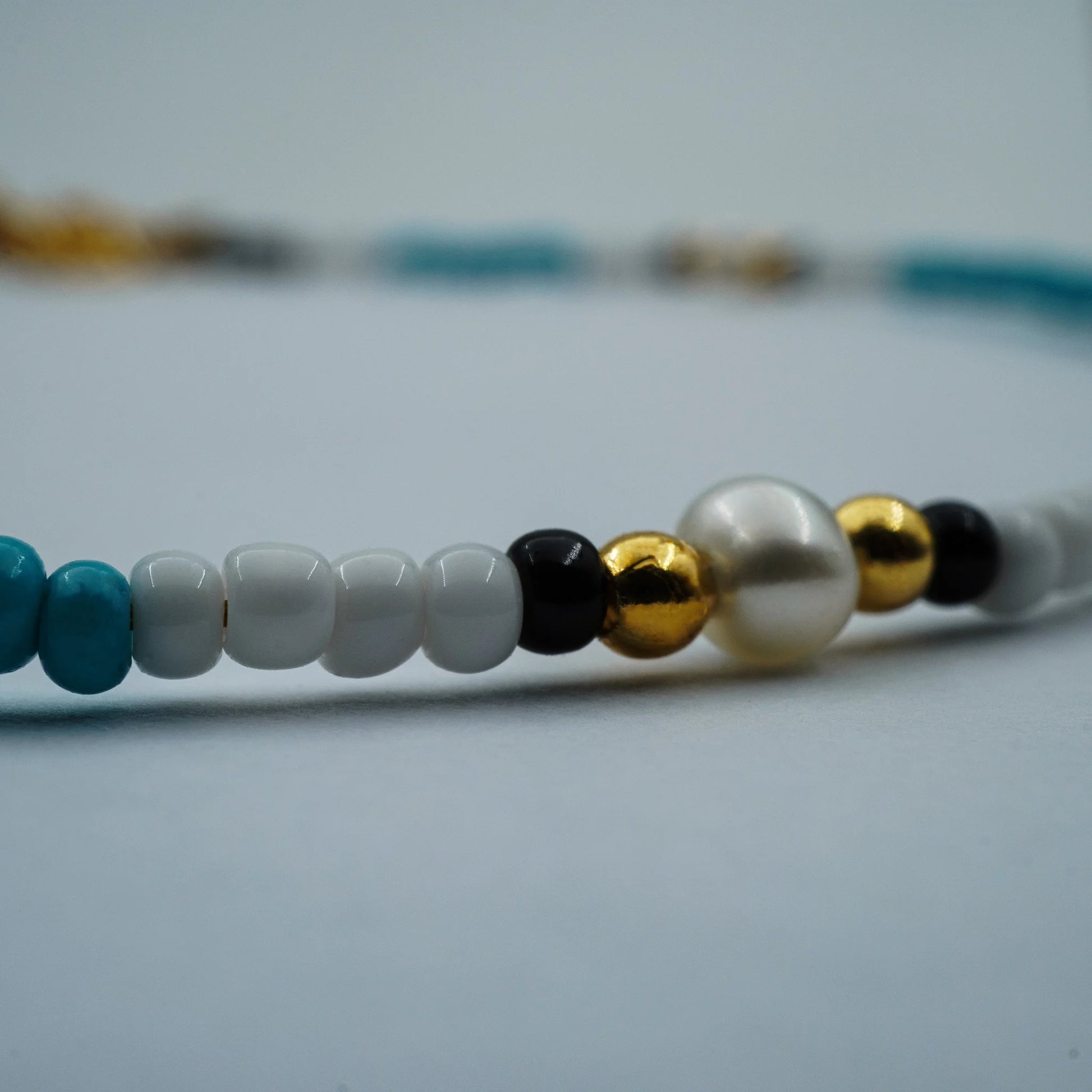 Close-up of handmade anklet showing pearls, blue beads, and gold details.