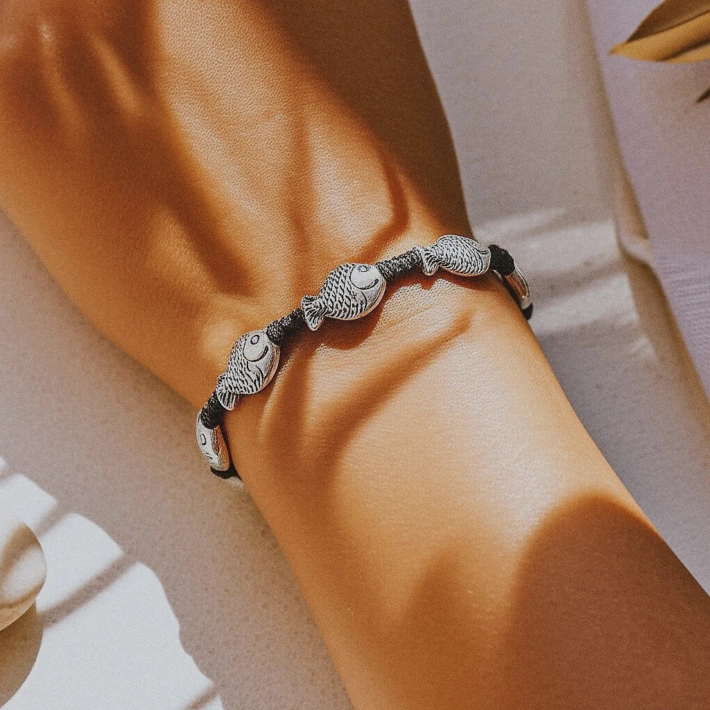 Woman wearing Camins Boho Spirit bracelet with tribal fish charms in a sunlit coastal setting, expressing handmade ocean-inspired style and beachside freedom.