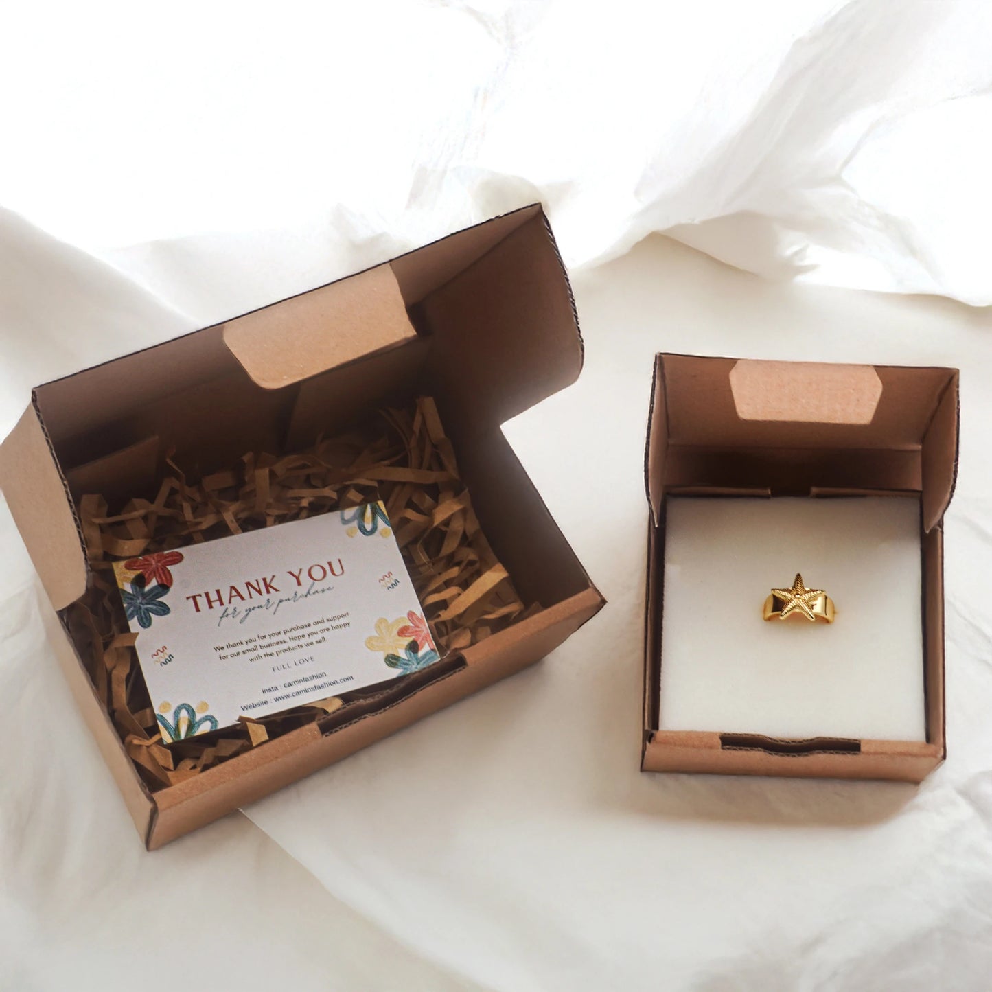 Camins Fashion star ring in gold-plated stainless steel, displayed in kraft jewelry packaging with thank-you card and soft linen background – Mediterranean coastal aesthetic.