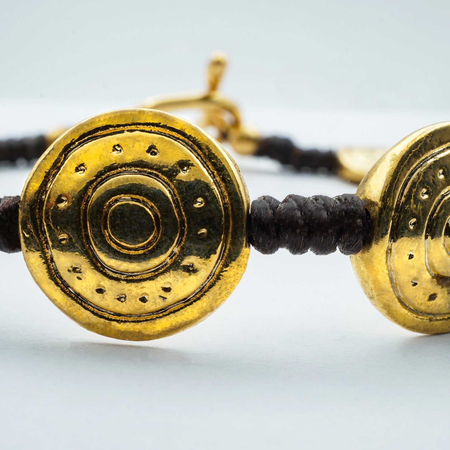 Close-up view of the Golden Spiral Medallion Bracelet featuring textured spiral charms with golden accents on a dark cord—handcrafted in Bali for an artisanal finish.