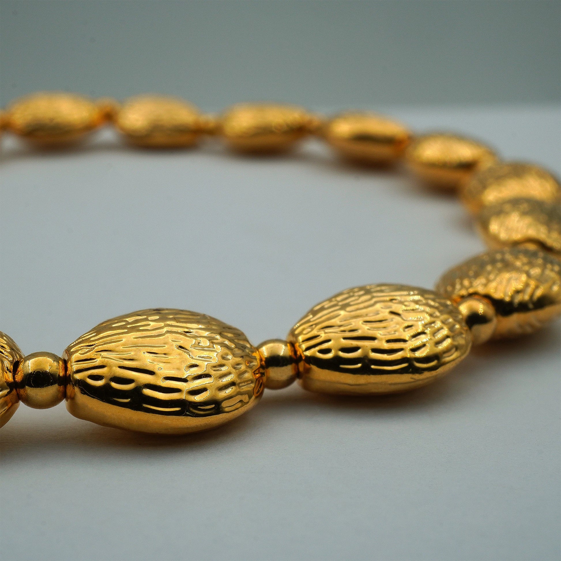 Close-up of textured oval gold-plated beads on the handmade bracelet, capturing fine craftsmanship and luminous detail