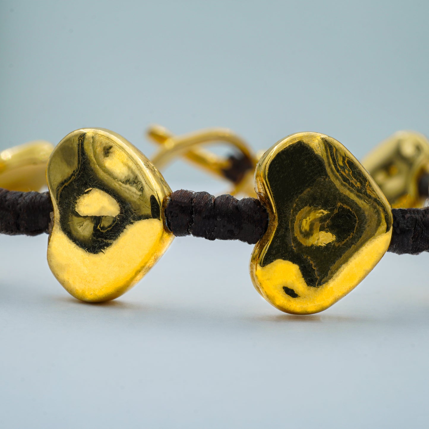 Close-up of Heart Bead Glow Bracelet showing smooth gold-tone heart charms and knotted cord detailing—highlighting the handcrafted elegance of Balinese jewelry.

