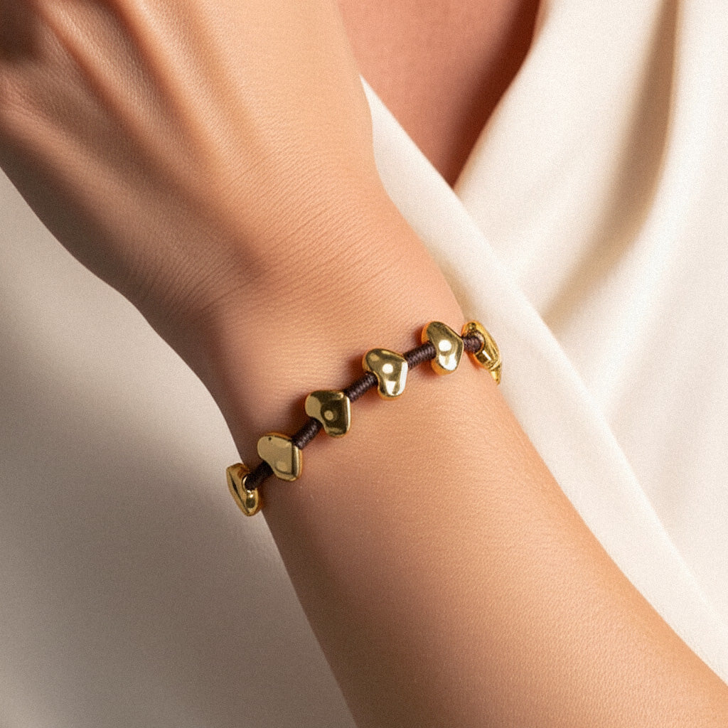 Model wearing the Heart Bead Glow Bracelet with golden heart-shaped beads on a dark cord—capturing a handmade Balinese charm in a warm, natural lifestyle setting.

