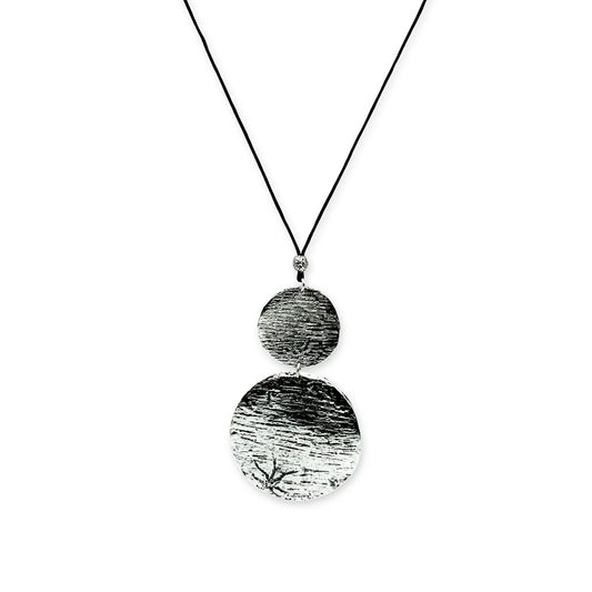 Front view of Lunar Balance Sliding Necklace by Camins Fashion – featuring two silver textured medallions on a black silk cord, evoking minimalist lunar harmony with a boho-modern touch.