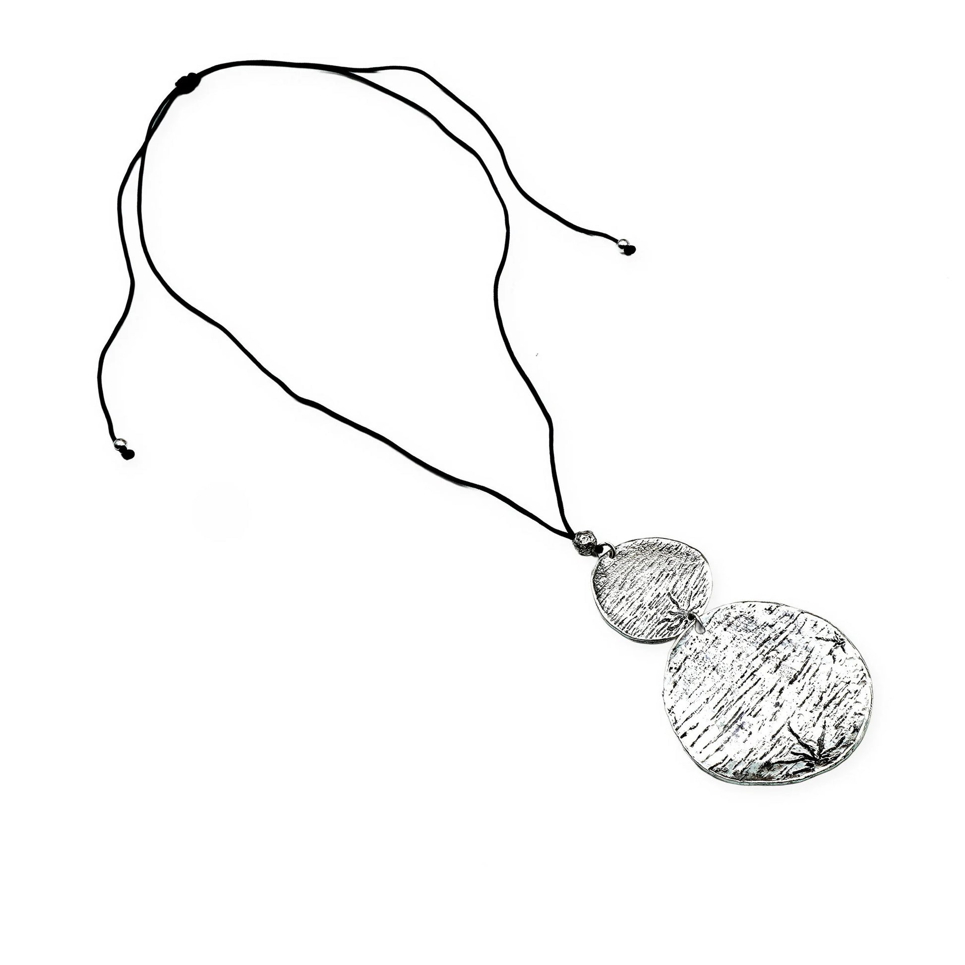 Top view of the Lunar Balance Sliding Necklace by Camins Fashion, showcasing two textured silver medallions connected on a smooth black silk cord — a handcrafted piece reflecting minimalist lunar symbolism and boho charm.