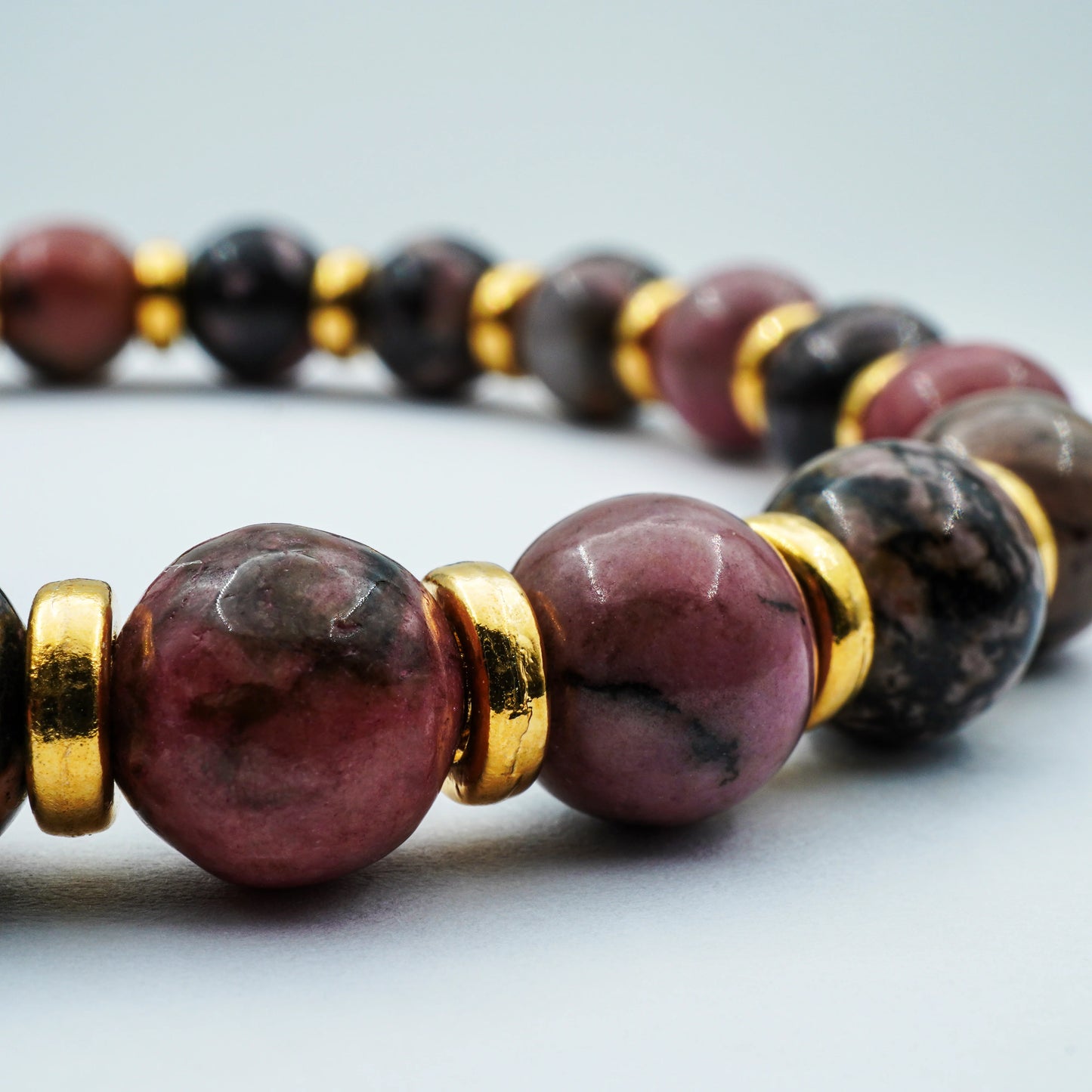 Close-up of polished Rhodonite beads on the handmade bracelet, highlighting the pink and maroon natural tones