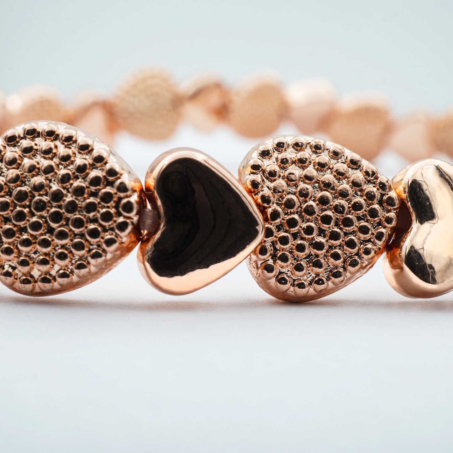 Close-up of the Rose Gold Heart Stretch Bracelet by Camins Fashion, highlighting alternating textured and polished heart beads in a romantic rose gold tone—handcrafted in Bali with minimalist charm.