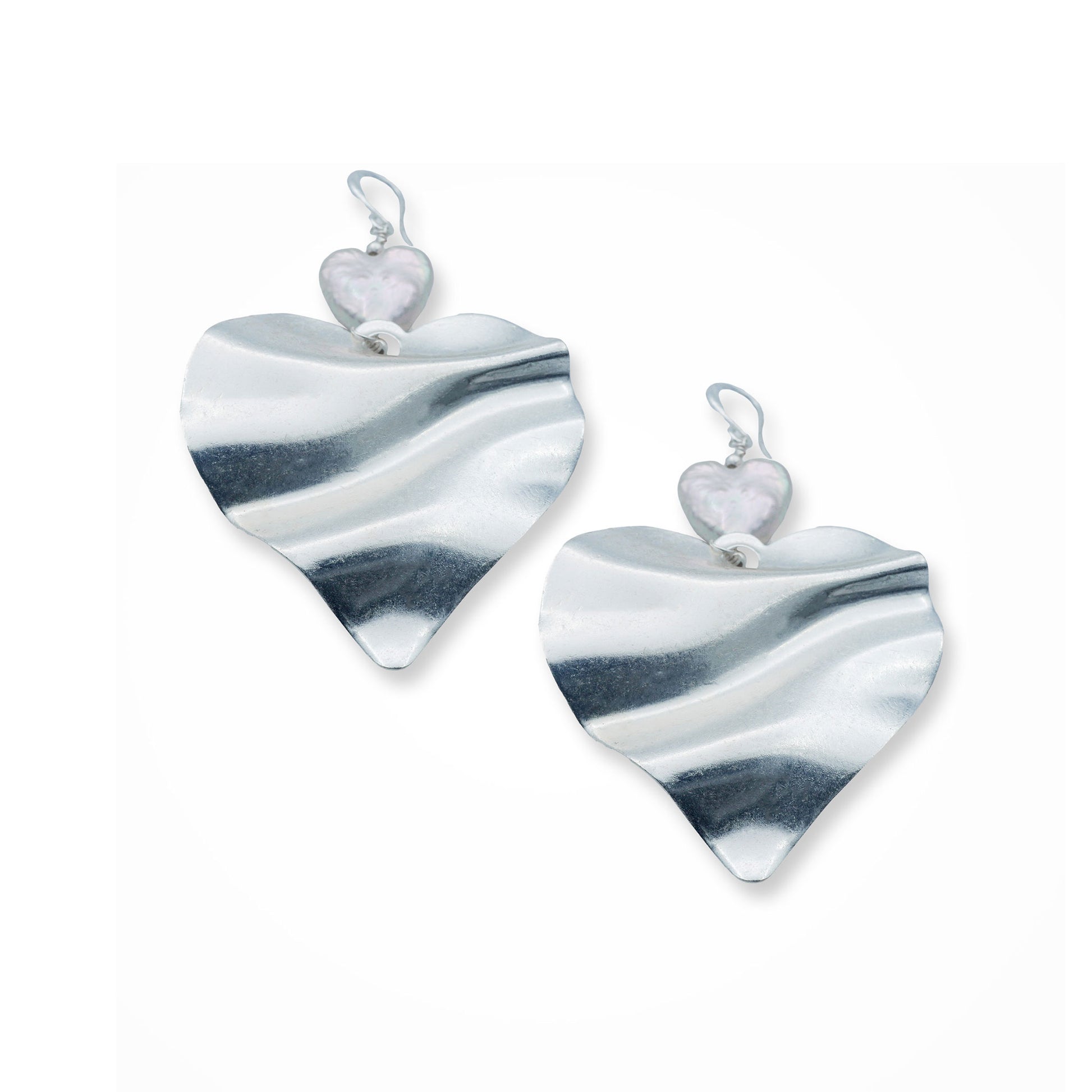 Close-up front view of a woman wearing silver heart pearl earrings with a sculptural double-heart design, capturing a bold romantic style in a soft Mediterranean light. Elegant statement jewelry with a modern boho twist.