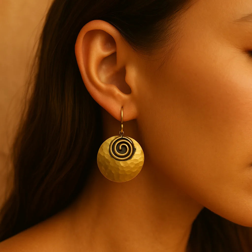 Close-up of a woman wearing hammered brass earrings with spiral detailing, radiating bold boho energy and warm Mediterranean charm, styled by Camins Fashion.
