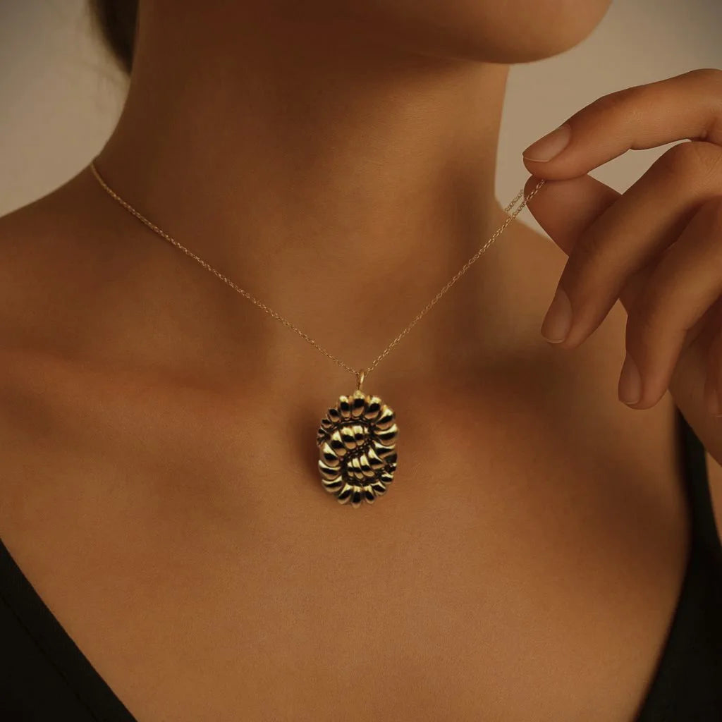 Close-up of a woman wearing a gold spiral shell pendant necklace on a delicate chain, capturing a textured, vintage-inspired design with Mediterranean-bohemian charm. The elegant styling and warm lighting enhance the necklace’s oceanic, sculptural beauty.