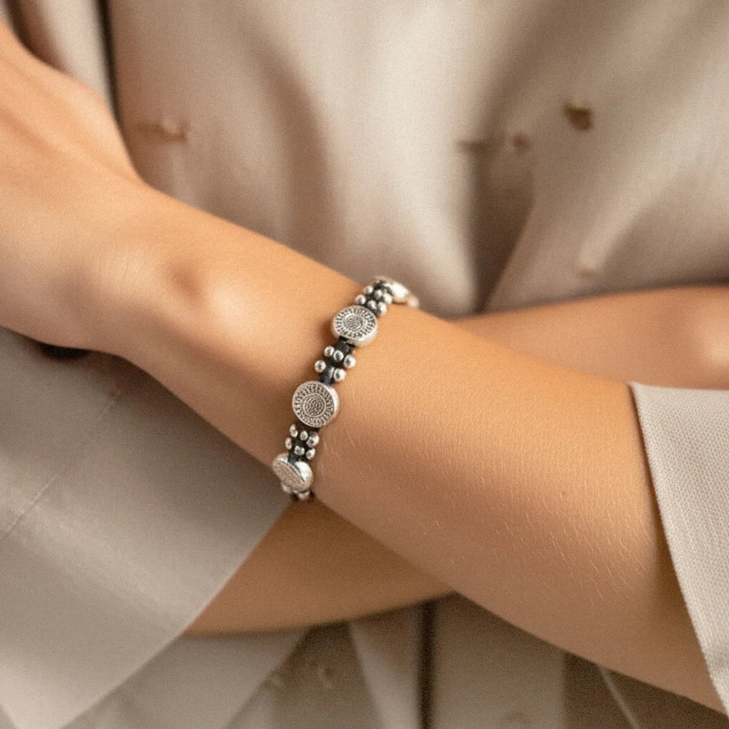 Woman’s hand wearing the Sunburst Charm Bracelet by the beach, showcasing handmade silver sun discs and tribal beads under natural tropical light.